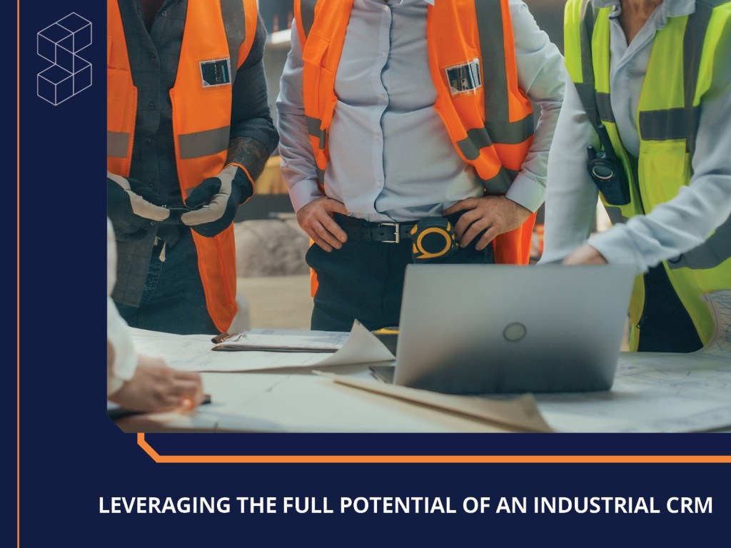 A group of professionals in safety vests discussing over a laptop and blueprints on a table, emphasizing teamwork and collaboration in an industrial setting.